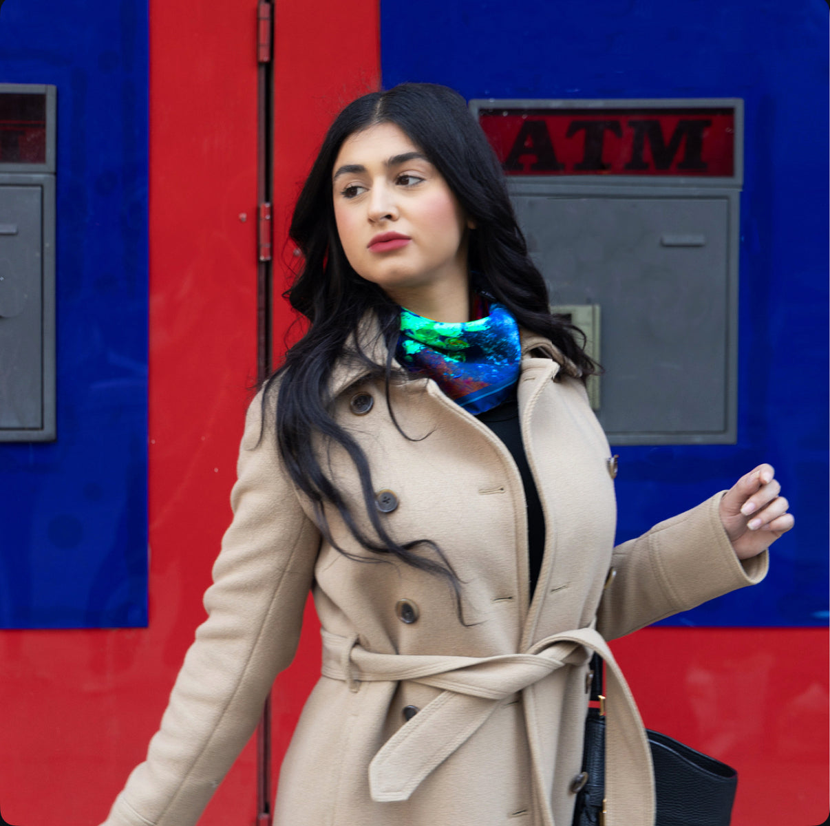 A beautiful girl wearing a Karnik by TK-LA scarf on her way to work or run errands. She has a camel coat and has the neckerchief tied around her neck. The vibrant colors of blue, cherry fire red, mustardy gold and seafoam bright green pop out and create a luxurious look to her everuyday outfit.