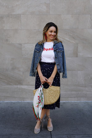 a cute girl wearing an Armenian t-shirt with red 70s writing that says lovely with polo dot skirt and denim jacket and a straw bag with a karnik by TK-LA scarf 